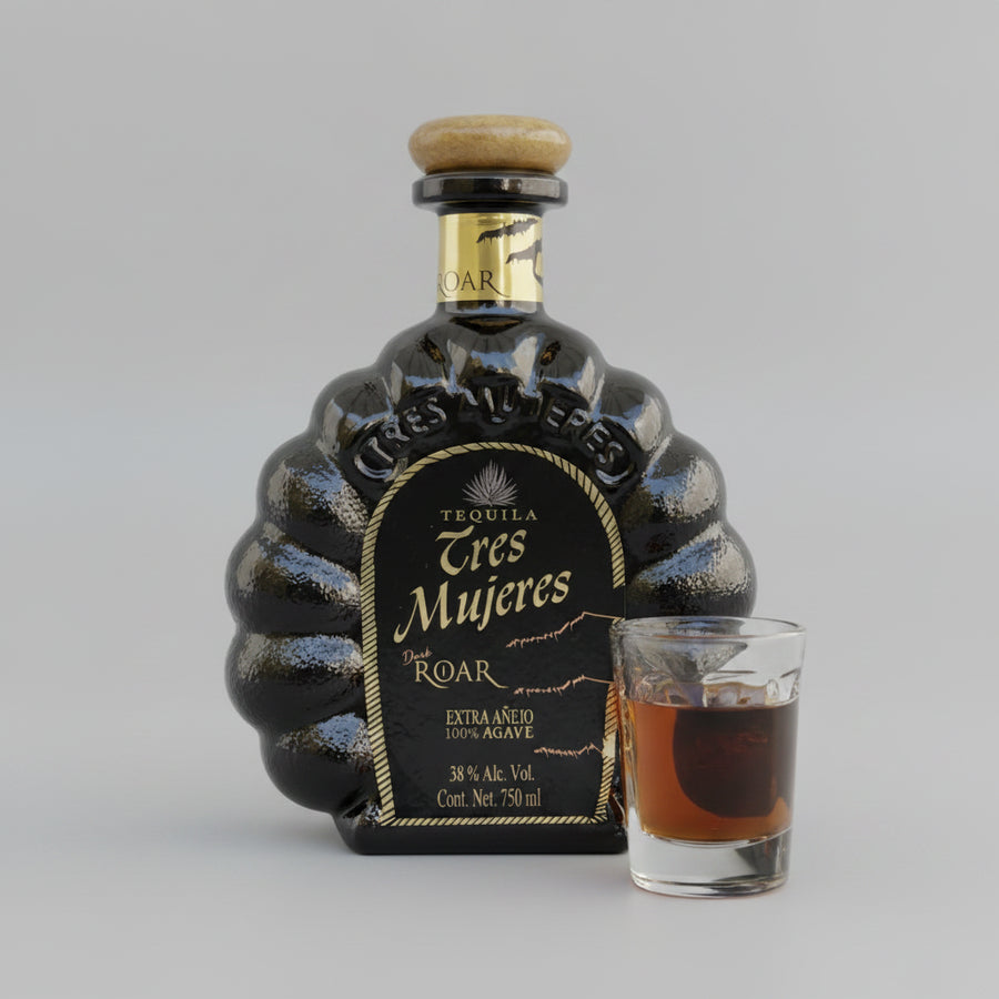 Bottle of Tres Mujeres Tequila with a glass of tequila on a wooden surface.