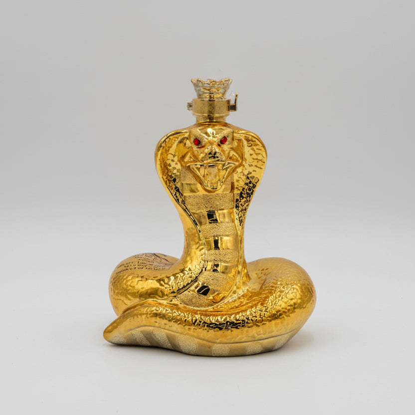 A sculptural bottle of Oceano Azul Golden Snake Añejo Tequila, featuring a coiled golden snake design with red eyes on the cap.